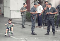 A child pedals past heavily-armed Police during the MRTA hostage crisis in Peru.