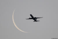 A passenger jet soars past a waning crescent moon at dawn.